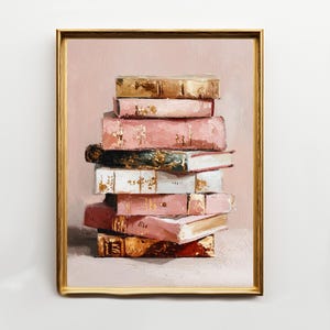 May include: A framed artwork featuring a stack of books. The books have pink, gold, and white covers, with gold accents. The background is a soft pink, and the frame is gold.