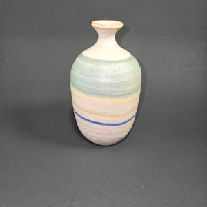 May include: A ceramic vase with a narrow neck and rounded body. The vase is primarily off-white with horizontal bands of light blue, yellow, and blue. The vase is a decorative item.