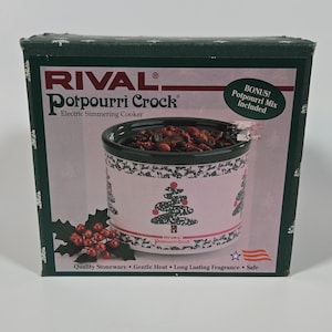 May include: A Rival Potpourri Crock electric simmering cooker in a box. The box features the product name, a graphic of the white stoneware crock with a black rim and Christmas tree pattern, red berries, and text including Quality Stoneware.