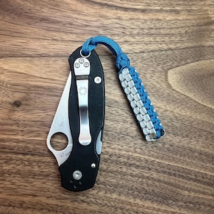May include: A black pocket knife with a silver blade and a blue and white paracord lanyard.