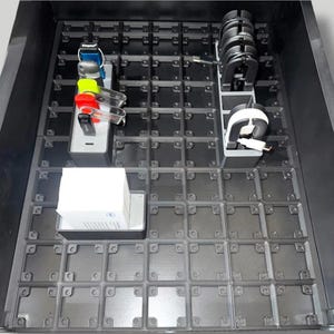 May include: A black modular drawer organizer tray with a grid pattern base. It includes three removable rectangular inserts: one holding several USB flash drives, one containing coiled charging cables, and one filled with a stack of white business cards.