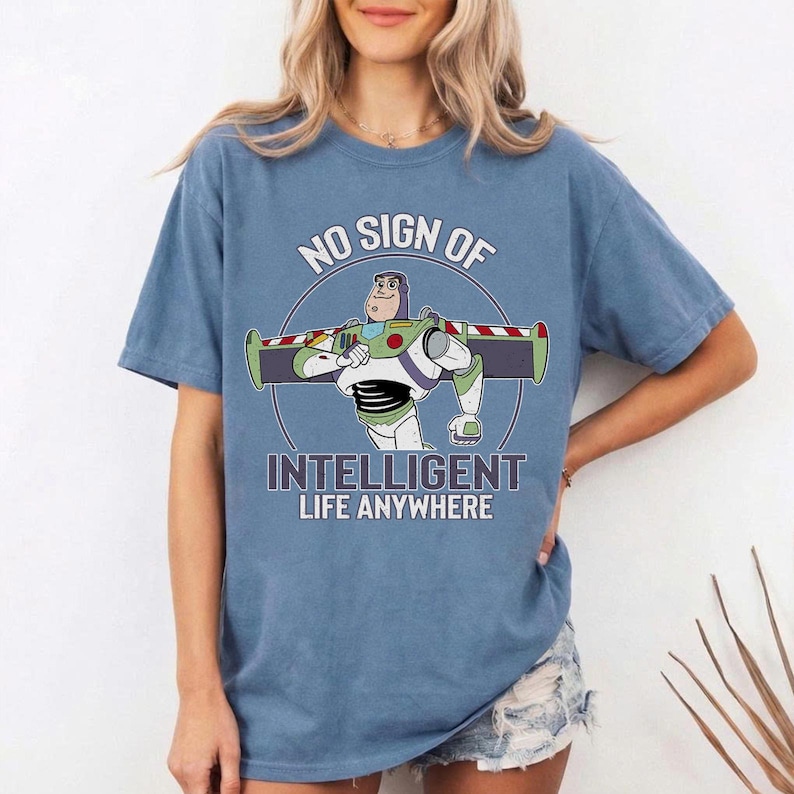 Puede incluir: Camiseta azul con un gr&aacute;fico de Buzz Lightyear y el texto "NO SIGN OF INTELLIGENT LIFE ANYWHERE". El dise&ntilde;o incluye un borde circular y los colores caracter&iacute;sticos del personaje.