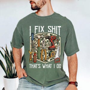 May include: Green t-shirt with the text "I FIX SHIT THAT'S WHAT I DO" and a graphic of various tools, including a hammer, screwdriver, drill, and saw. The tools are set against a camouflage background.
