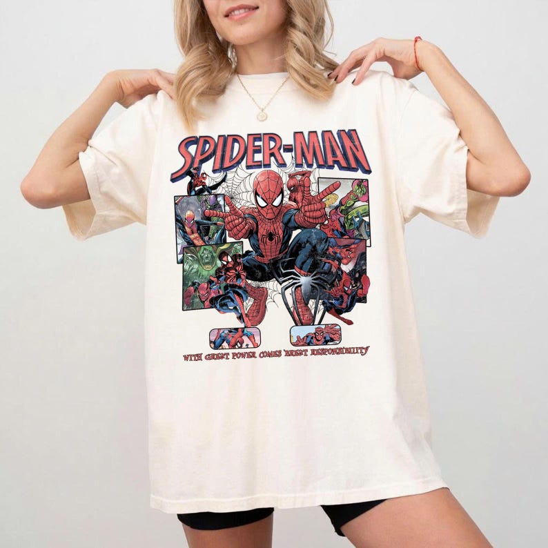 May include: Cream-colored t-shirt featuring a Spider-Man graphic. The design includes the words "Spider-Man" in red and blue, along with comic book panels of Spider-Man in action. The phrase "With great power comes great responsibility" is printed below.