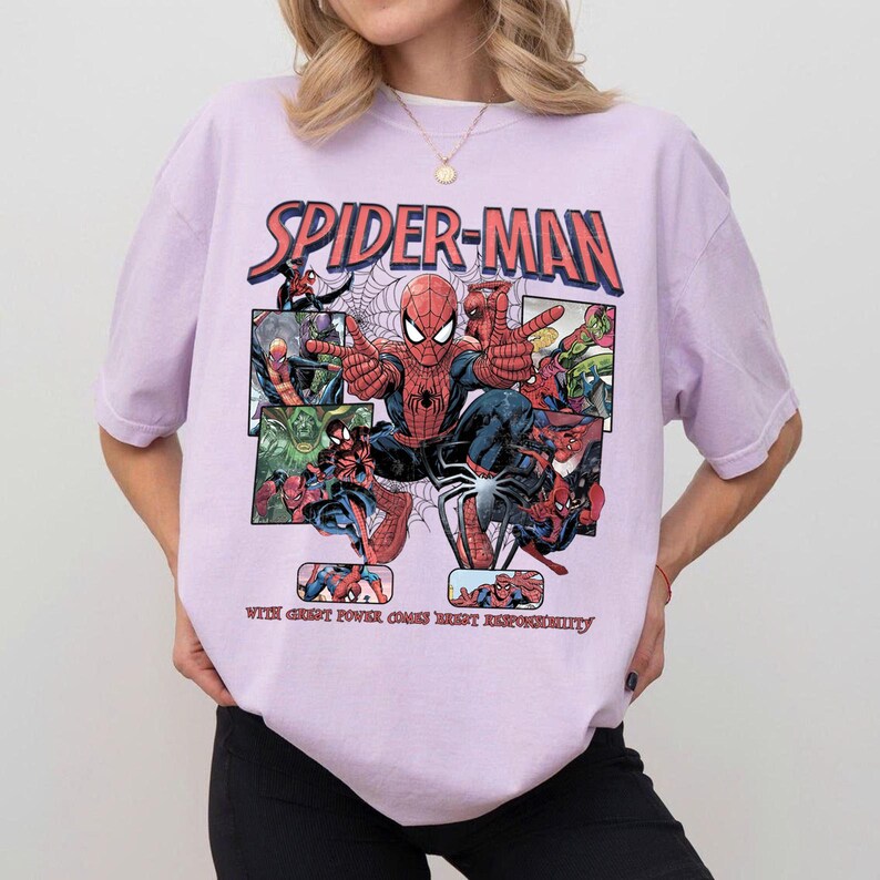 May include: A light purple t-shirt featuring a Spider-Man graphic. The design includes the words "SPIDER-MAN" in red and blue, along with comic book panels and the phrase "WITH GREAT POWER COMES GREAT RESPONSIBILITY."
