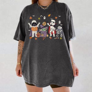 Op de afbeelding: Een antracietgrijs T-shirt met korte mouwen en een grafische print van Star Wars-personages verkleed voor Halloween, waaronder een mummie, een heks, een vampier en een skelet, omringd door kleine spookjes, blaadjes en snoepjes.