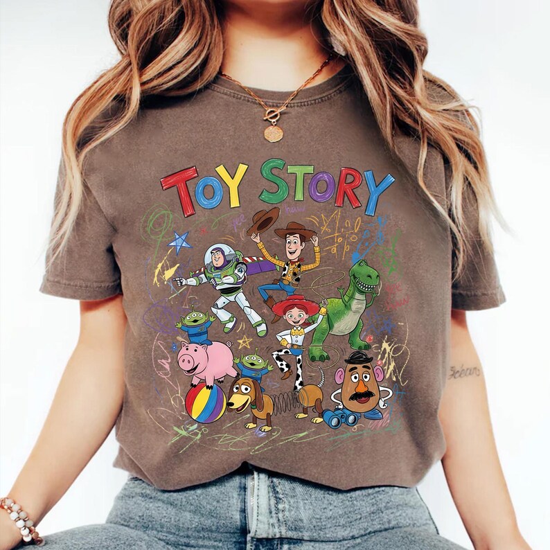 May include: Brown t-shirt featuring the words "TOY STORY" in colorful letters above a graphic of characters from the animated film. The design includes Buzz Lightyear, Woody, Jessie, Rex, and other characters.