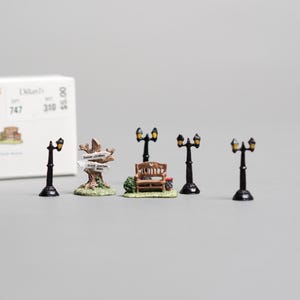 May include: Miniature accessory set from The Americana Collection. Includes six miniature lampposts, a park bench, and a signpost. The set also includes a small statue. The box reads "Six Miniature Accessory Set".