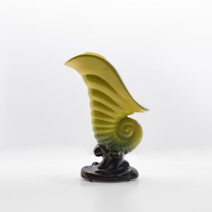 May include: A decorative vase in the shape of a nautilus shell. The vase features a spiral design with a yellow-green gradient and a dark base. The shell-shaped vase is a unique home decor item.