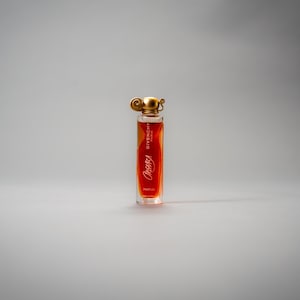 May include: A clear glass perfume bottle with a gold-colored cap and a red label. The label features the brand name "Givenchy" and the perfume name "Organza" in a stylized font. The bottle is filled with a light orange liquid.