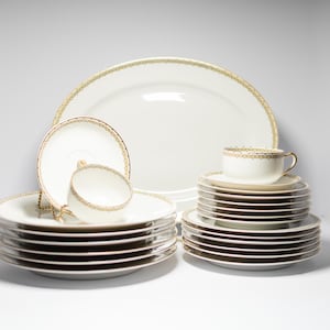 Può includere: Un servizio di piatti in porcellana bianca con bordi dorati. Il set include un grande piatto ovale, piatti, piattini e tazze da tè. I bordi dorati decorano i bordi dei piatti e delle tazze, creando un aspetto elegante e classico.