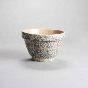 May include: A ceramic mixing bowl with a cream-colored interior and a speckled blue and beige exterior. The bowl has a wide rim and a rounded shape, perfect for kitchen use. The bowl is approximately 6 inches in diameter and 4 inches tall.