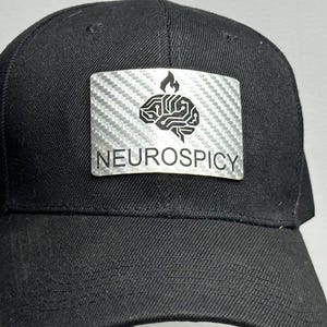 May include: Black baseball cap with a curved brim. A silver patch on the front displays a brain graphic with a flame above it and the word "NEUROSPICY" in white text. The cap is made of a durable fabric.