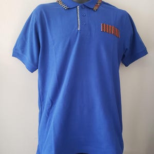 May include: A royal blue polo shirt with short sleeves. The collar and pocket feature a colorful, patterned design. The shirt has a three-button placket and a decorative stitch detail.