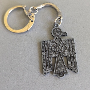 May include: A silver-colored metal keychain featuring a stylized bird design. The bird has a geometric pattern and is attached to a key ring and a coiled metal chain.