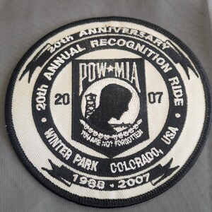 May include: A circular patch with black and white embroidered text and graphics. The patch commemorates the 20th Annual Recognition Ride in Winter Park, Colorado, USA, from 1988-2007. The central design includes the text "POW-MIA" and a silhouette.