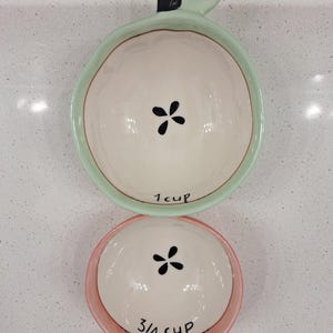 Pu&ograve; includere: Set di tre misurini in ceramica a forma di mela. La tazza superiore &egrave; verde e contrassegnata con "1 cup". La tazza centrale &egrave; rosa e contrassegnata con "3/4 cup". Ogni tazza presenta un motivo floreale nero al centro.