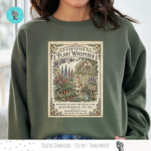 May include: Olive green sweatshirt featuring a vintage-style graphic. The graphic reads "Certified Plant Whisperer" and depicts a rabbit tending a garden with flowers and a small house. The text "Selective Seed Co. | Est. 1923" is also included.