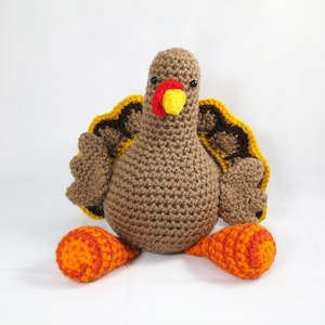 Puede incluir: Un juguete de peluche de pavo tejido a crochet con hilo marrón, amarillo y naranja. El pavo tiene un pico rojo y amarillo y ojos negros.