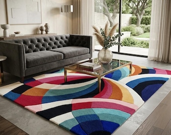 May include: A rectangular area rug featuring a bold, multi-colored geometric pattern of overlapping circular arcs in shades of deep blue, teal, magenta, orange, yellow, and cream, laid out on a floor in a living room setting with a sofa.