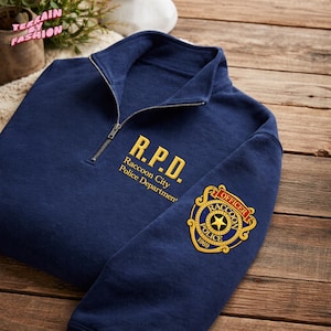May include: Navy blue quarter-zip sweatshirt with gold embroidered text reading "R.P.D. Raccoon City Police Department." A gold and blue patch on the sleeve reads "Officer Raccoon Police 1969."