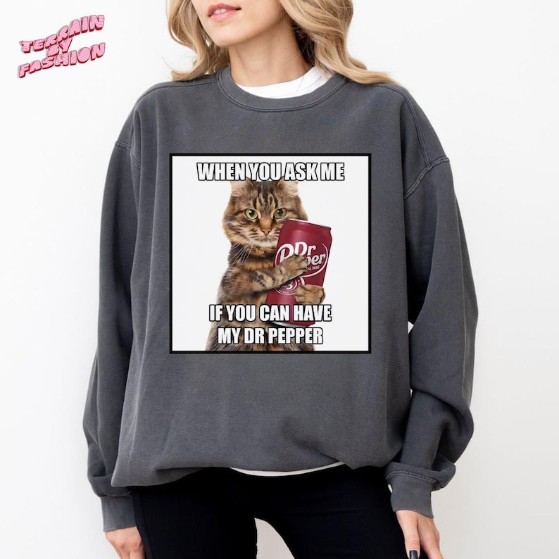 May include: Dark grey sweatshirt featuring a humorous graphic of a cat holding a Dr. Pepper can. The text on the graphic reads "WHEN YOU ASK ME IF YOU CAN HAVE MY DR PEPPER". The sweatshirt has a crew neck and long sleeves.