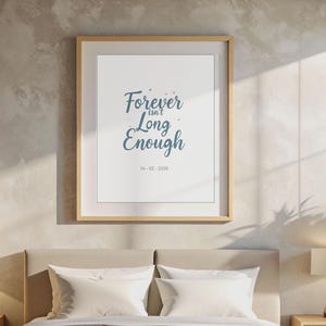 Puede incluir: Interior de dormitorio con una cama con ropa de cama blanca y una colcha gris. Dos mesitas de noche con lámparas flanquean la cama. Una impresión enmarcada en la pared muestra el texto "Forever isn't Long Enough". También se ve una planta en maceta.