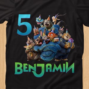 May include: Black t-shirt featuring a colorful graphic of cartoon animals, a blue number 5, and the name BENJAMIN in green and blue. The design includes characters with party hats and gifts, suitable for a birthday celebration.