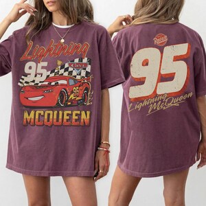 May include: A maroon t-shirt featuring a graphic of Lightning McQueen from the movie Cars. The front design includes the text "Lightning 95 McQueen" with an image of the race car. The back of the shirt displays a large "95" and "Lightning McQueen" text.