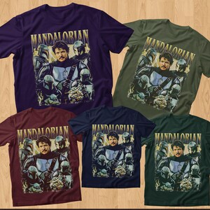 May include: Five short-sleeved t-shirts in various colors: purple, olive green, burgundy, navy blue, and dark green. Each shirt features a graphic of a man and several figures in helmets, with the word "MANDALORIAN" in gold lettering.