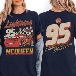 May include: Navy blue t-shirt featuring a graphic of Lightning McQueen from the Cars movie. The front design includes the text "Lightning 95 McQueen" with a red race car. The back of the shirt displays the number "95" and "Lightning McQueen".
