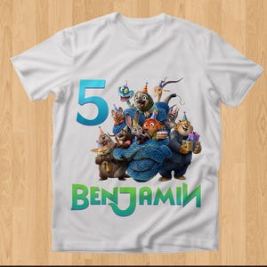 May include: White t-shirt featuring a colorful graphic of animated animal characters, a large teal number 5, and the name "BENJAMIN" in green. The design includes a birthday cake and wrapped gifts.