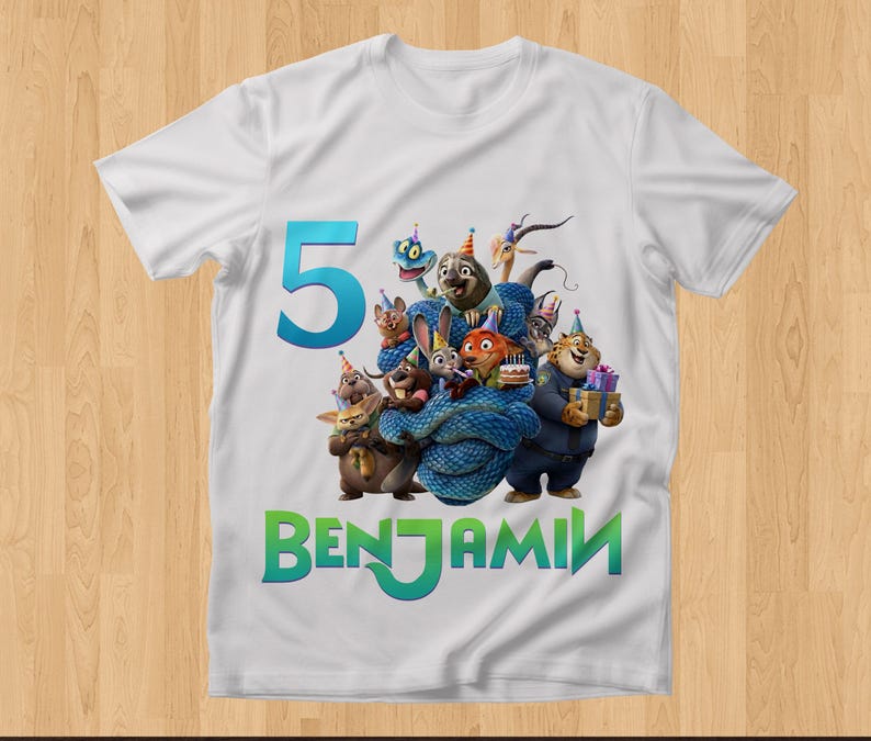 May include: White t-shirt featuring a colorful graphic of animated animal characters, a large teal number 5, and the name "BENJAMIN" in green. The design includes a birthday cake and wrapped gifts.