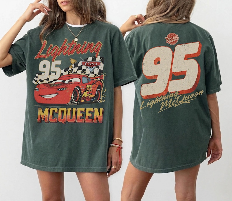 May include: Dark green t-shirt featuring a graphic of Lightning McQueen from the Cars movie. The front design includes the text "Lightning 95 McQueen" with a red race car. The back displays "95 Lightning McQueen".