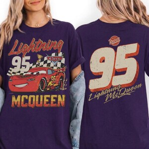 May include: Purple t-shirt featuring a graphic of Lightning McQueen from the Cars movie. The front design includes the number 95, the text "Lightning McQueen," and a checkered flag. The back of the shirt also displays the number 95 and the text "Lightning McQueen."