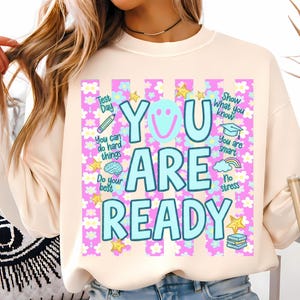 May include: A cream-colored sweatshirt with a graphic design that reads "YOU ARE READY" in light blue letters. The design includes a smiley face, stars, and encouraging phrases like "Do your best" and "You are smart."