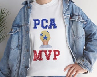 Puede incluir: Una camiseta blanca con el texto azul PCA, un gráfico de una persona con cabello rubio y estrellas azules, y el texto rojo MVP. La camiseta se lleva debajo de una chaqueta vaquera azul con botones metálicos y se combina con vaqueros azules.
