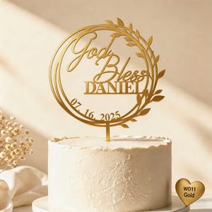 Può includere: Un cake topper dorato con le parole "God Bless DANIEL" e la data "07. 16. 2025" è esposto su una torta bianca. Il topper ha un design circolare con una ghirlanda di foglie. Un'etichetta dorata a forma di cuore è a destra.