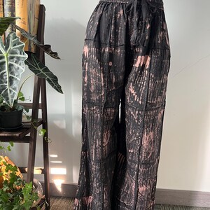 Puede incluir: Pantalones anchos negros y rosas teñidos con un cinturón elástico y cordón. Los pantalones tienen un diseño de patchwork y están hechos de una tela ligera. Los pantalones se exhiben en un maniquí.
