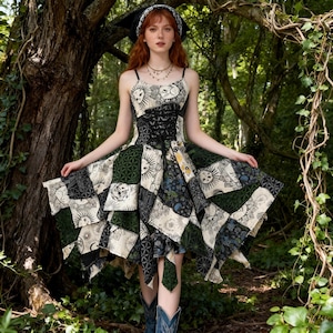 Puede incluir: Vestido patchwork con corpiño negro estilo corsé y tirantes finos. El vestido presenta una mezcla de telas estampadas en crema, verde y negro, con motivos de sol y luna. El vestido tiene un dobladillo asimétrico.