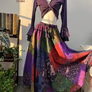 Peut inclure: Ensemble deux pièces composé d'un haut à manches longues violet foncé avec des manches évasées et d'une jupe longue patchwork. La jupe présente une variété de motifs de tissus colorés, notamment des motifs floraux et géométriques. Le haut a un détail torsadé sur le devant.