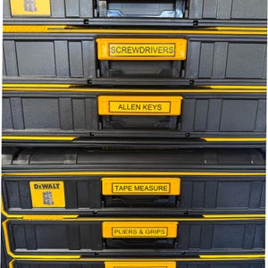 May include: Black and yellow tool storage system with labelled drawers. Labels include "SCREWDRIVERS", "ALLEN KEYS", "TAPE MEASURE", and "PLIERS & GRIPS". The brand name "DEWALT" is visible on one drawer.