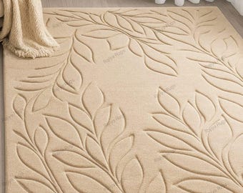 May include: Beige rectangular area rug with a raised leaf pattern. The rug has a soft, textured appearance and is placed on a light-colored wooden floor. A beige throw blanket is draped over a chair in the background.