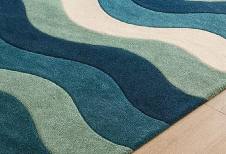 May include: A rectangular rug with a wave pattern in shades of blue, teal, and white. The rug has a soft, textured appearance, with the wave design creating a sense of movement. The rug is placed on a light-colored wooden floor.