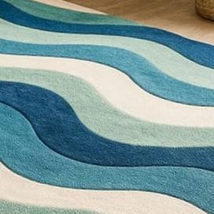 May include: A rug with a wave pattern in shades of blue and white. The rug's design features flowing, curved lines, creating a textured surface. The rug is made of a soft material, suitable for a living room or bedroom.