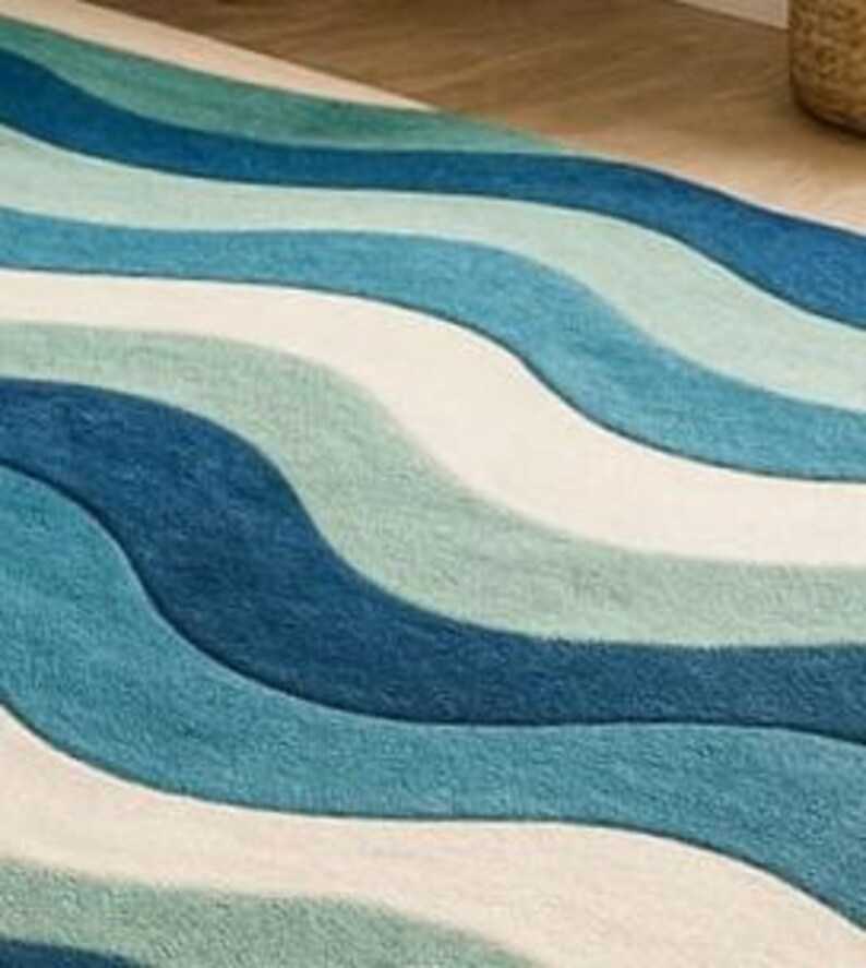 May include: A rug with a wave pattern in shades of blue and white. The rug's design features flowing, curved lines, creating a textured surface. The rug is made of a soft material, suitable for a living room or bedroom.