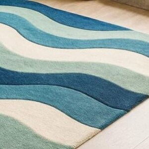 May include: A rectangular rug with a wave pattern in shades of blue and off-white. The rug's design features flowing, curved lines that create a sense of movement. The rug is made of a soft material, and the colors are evenly distributed across the surface.
