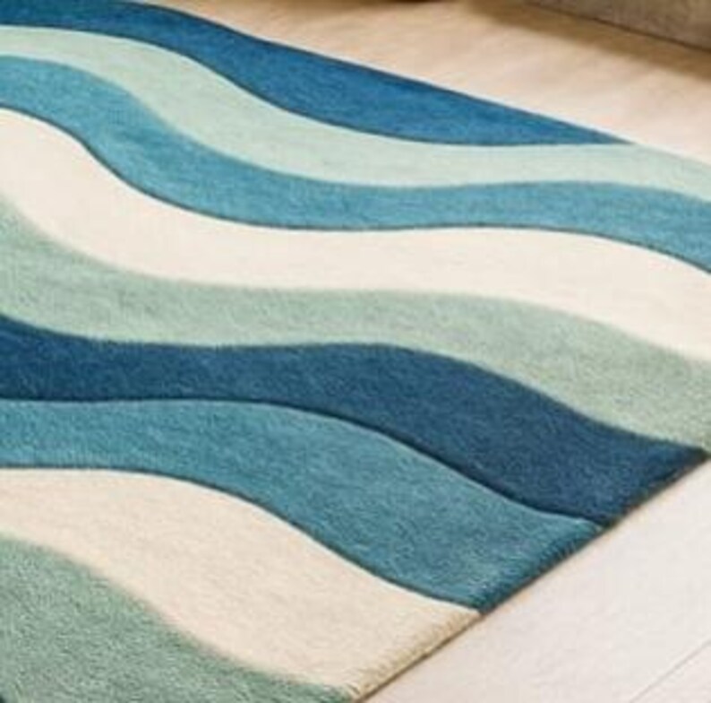 May include: A rectangular rug with a wave pattern in shades of blue and off-white. The rug's design features flowing, curved lines that create a sense of movement. The rug is made of a soft material, and the colors are evenly distributed across the surface.