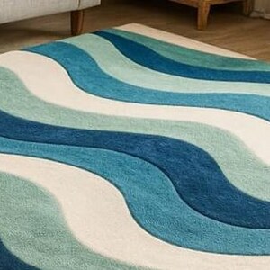May include: A rectangular rug with a wavy pattern in shades of blue, teal, and off-white. The rug's design features broad, flowing stripes that create a sense of movement and texture. The rug is made of a soft, plush material.