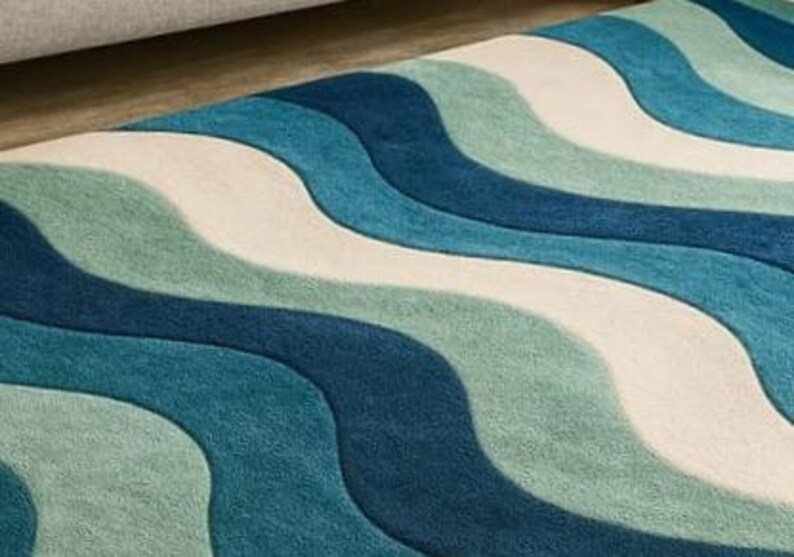 May include: A close-up of a rug with a wavy pattern in shades of blue, teal, and white. The rug has a soft, textured appearance, with the waves flowing across the surface. The rug is a home decor item.